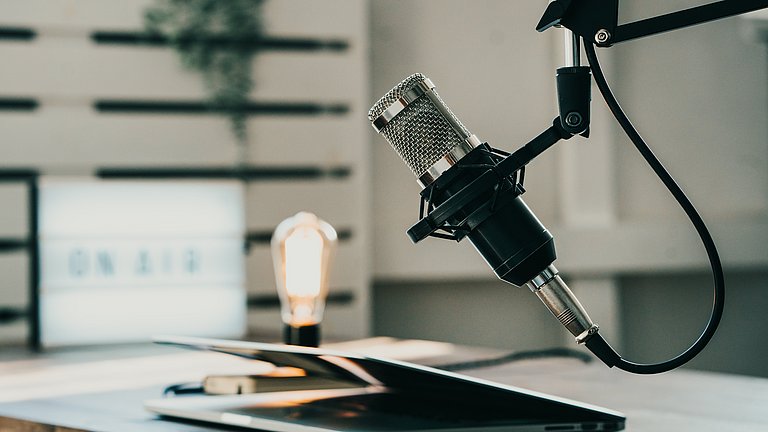 Ein Heimstudio für die Produktion von Podcasts mit Mikrophon und zugeklapptem Laptop.