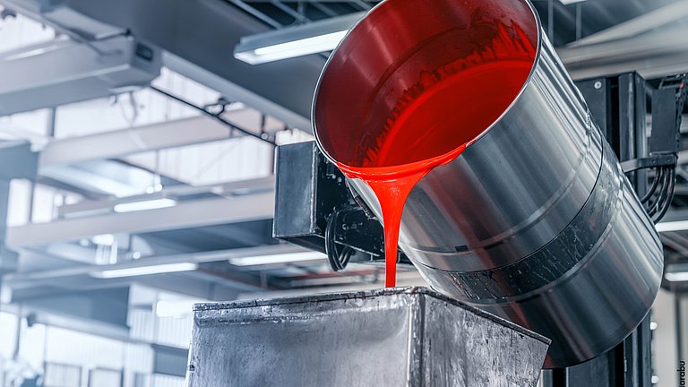 In einer hellen Produktionshalle fließt aus einem großen Metallfass rote Farbe in den Container einer Abfüllanlage.