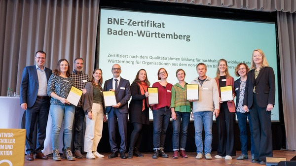 Die Empfängerinnen und Empfänger der BNE-Zertifikate stehen gemeinsam mit der Umweltministerin Thekla Walker und Staatssekretär im Kultusministerium Volker Schebesta stehen gemeinsam zum Gruppenbild auf der Bühne des Netzwerkforums BNE-BW 2030.