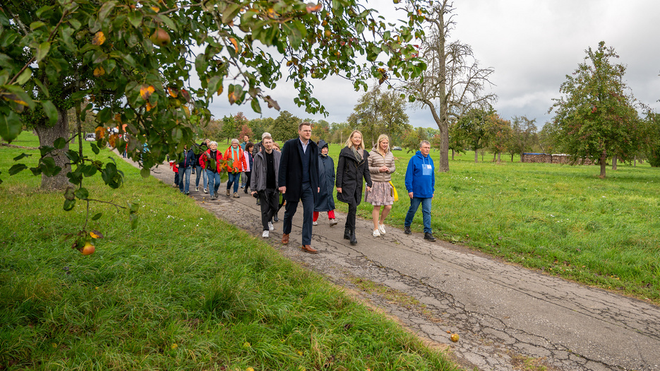 Umweltministerin Thekla Walker, die Streuobstwiesenkönig und ein Tross Besucher gehen entlang der neu eingeweihten Streuobstwiesenlehrpfades im Rahmen der Klimaländtage. 