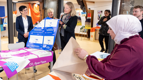 Umweltministerin Thekla Walker, Oberbürgermeisterin von Metzingen Carmen Haberstroh, Landtagsabgeordnete Cindy Holmberg und weitere Besucher des Nähcafes Metzingen begutachten aussortierte Banner der Nachhaltigkeitsstrategie Baden-Württemberg.