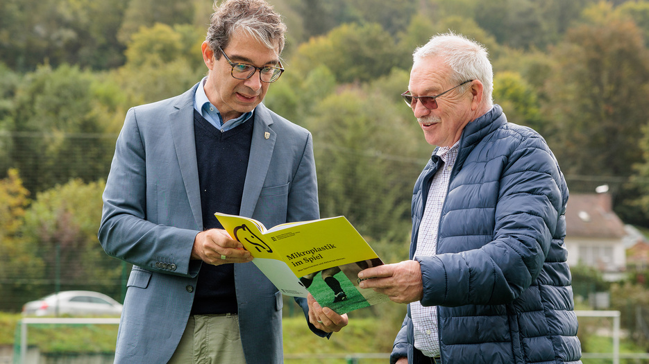 Staatssekretär Dr. Andre Baumann in Heiligkreuzsteinach zu Besuch auf dem Sportplatz und im Gespräch über die Broschüre zum Thema "Mikroplastik im Spiel".